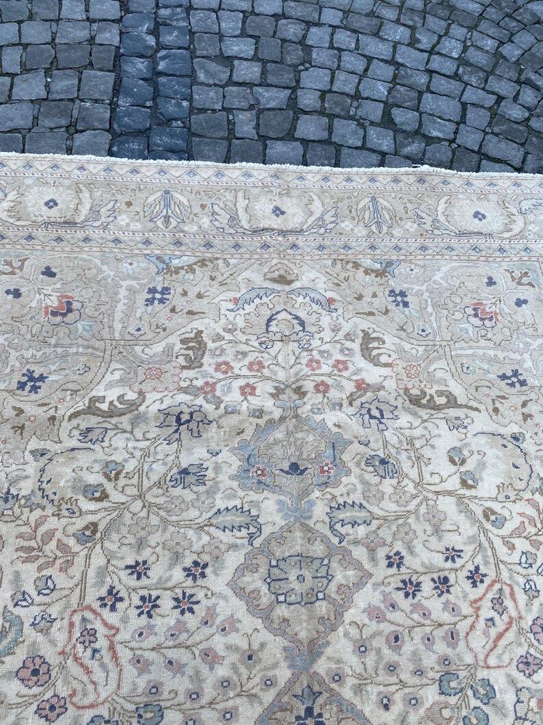 May include: A cream-coloured rug with a floral pattern in shades of blue, pink, and brown. The rug has a border with a repeating design.