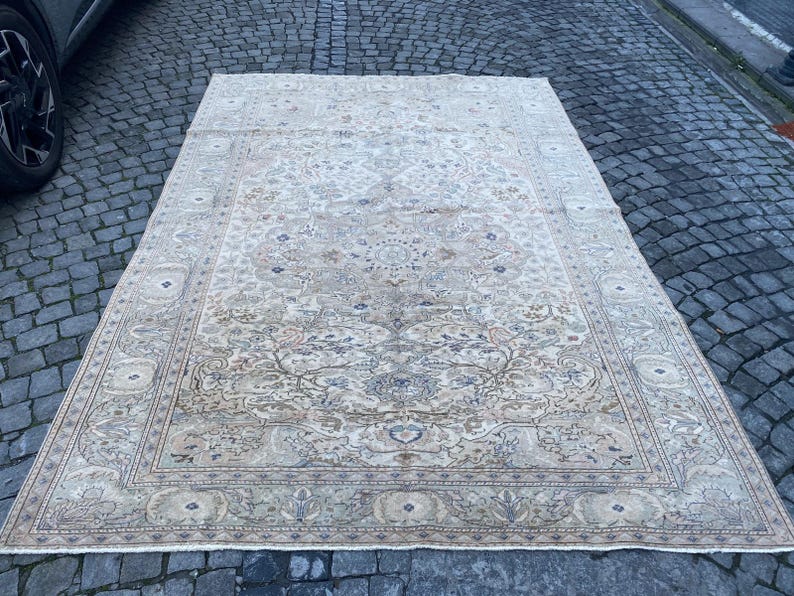 May include: A large, cream-coloured rug with a floral pattern. The rug has a detailed border with a repeating design.