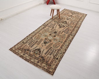 May include: A beige runner rug with a floral pattern in shades of brown, green, and blue. The rug has a fringed edge and is laid out on a white floor.