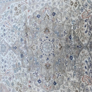 May include: A beige rug with a detailed floral pattern in shades of blue, brown, and pink. The rug has a central medallion with a circular design.