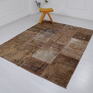 May include: A patchwork rug with a variety of brown and beige tones. The rug is made of different pieces of fabric sewn together, creating a unique and interesting design. The rug is laid out on a white floor with a small wooden stool in the background.