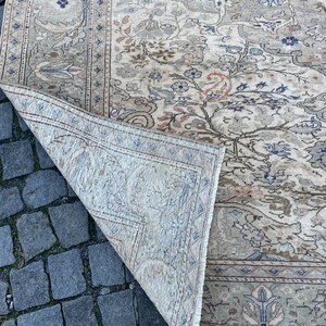 May include: A beige rug with a floral pattern in shades of brown, blue, and pink. The rug has a fringed edge and is folded in half.