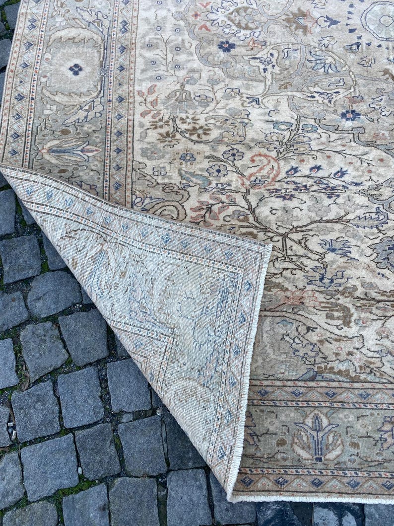 May include: A beige rug with a floral pattern in shades of brown, blue, and pink. The rug has a fringed edge and is folded in half.