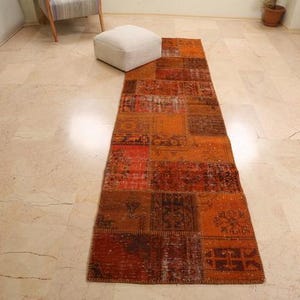 May include: A long, rectangular patchwork rug with a variety of colors and patterns. The rug is made up of different pieces of fabric sewn together, creating a unique and eclectic look. The rug is mostly orange and red, with some brown and blue accents.