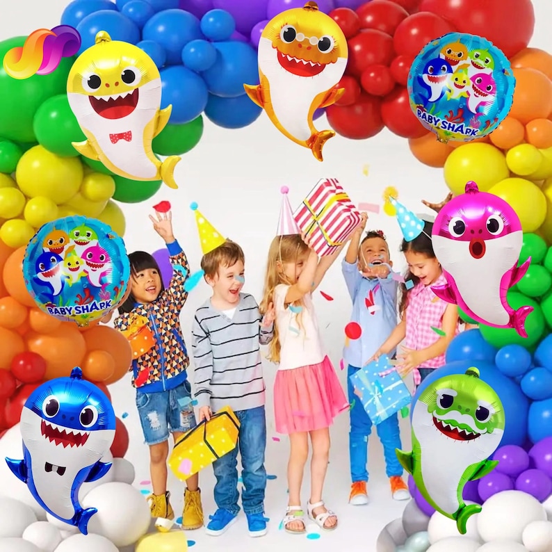 K&ouml;nnte beinhalten: Eine festliche Szene mit feiernden Kindern, umgeben von bunten Luftballons. Haif&ouml;rmige Folienballons und runde Ballons mit dem Text "Baby Shark" sind prominent. Kinder halten Geschenke und tragen Partyh&uuml;te.