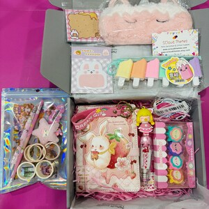 Op de afbeelding: Een briefpapier-cadeaubox met een pluche eenhoorn-etui, een notitieboek met een konijn- en aardbeienafbeelding, een pen met een poppenbedel, ijsvormige gummen, donutvormige gummen, washi-tape rollen, stickers en een memoblok.