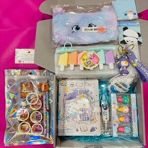 Op de afbeelding: Een briefpapier-cadeauset met een pluizig pastelkleurig etui, een notitieboek met een eenhoornthema, gummen in de vorm van ijsjes, een panda-notitieblok, een sleutelhanger, rollen washi-tape, decoratieve stickers en kleurrijke pennen.