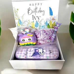 May include: A white gift box containing a purple pencil case with a Kuromi character print, a multi-color pen with a character topper, a purple pop-it toy, and a sheet of stickers. The lid features floral illustrations and the text Happy Birthday Ivy.