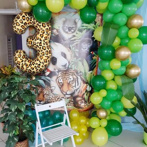 May include: A green, yellow, and gold balloon arch with a large leopard print number 3 balloon in front of a jungle animal themed backdrop.