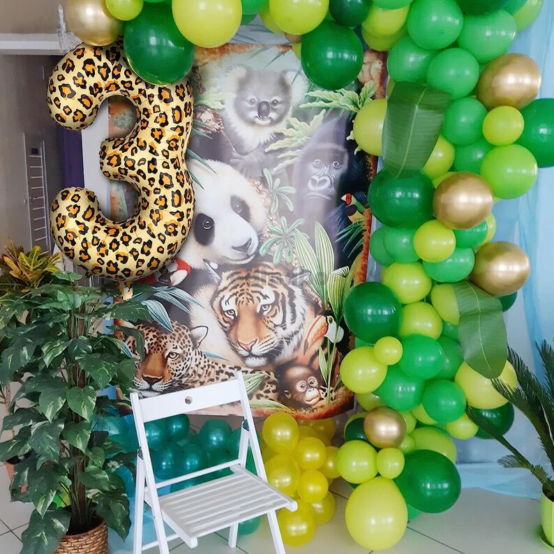 May include: A green, yellow, and gold balloon arch with a large leopard print number 3 balloon in front of a jungle animal themed backdrop.