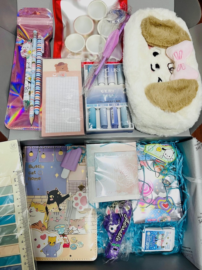 Op de afbeelding: Een briefpapier-cadeaubox met een pluche wit en bruin etui met een roze strik, een set pennen, een ruitjesblok met een berenicoon, een liniaal van 13 cm, een notitieboek met kattenillustraties, stickers en diverse kantoorbenodigdheden.