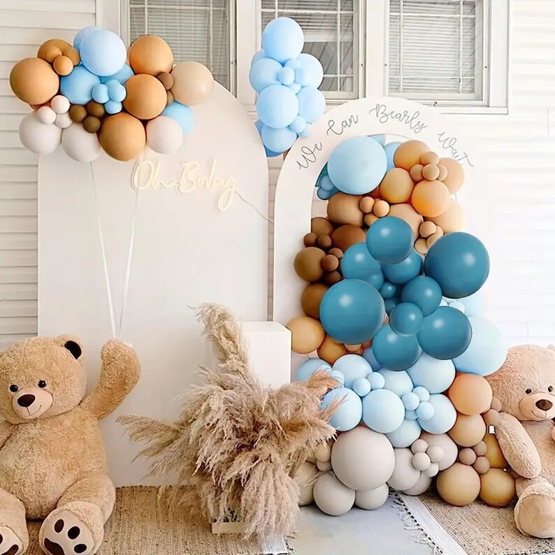 Pode incluir: Um arco de bal&otilde;es azul, marrom e branco com o texto "We Can Barely Wait" e "Oh Baby" em luzes de n&eacute;on. Dois ursos de pel&uacute;cia est&atilde;o de cada lado do arco.