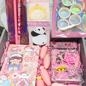 Op de afbeelding: Een briefpapier-cadeaubox met een roze pen met varkentje, een potlood, een Baby Panda notitieblok, vijf rollen washi-tape, een Yawan's Fairy notitieboek, vier wortelvormige items, een doosje taartvormige gummen en een mini correctietape.