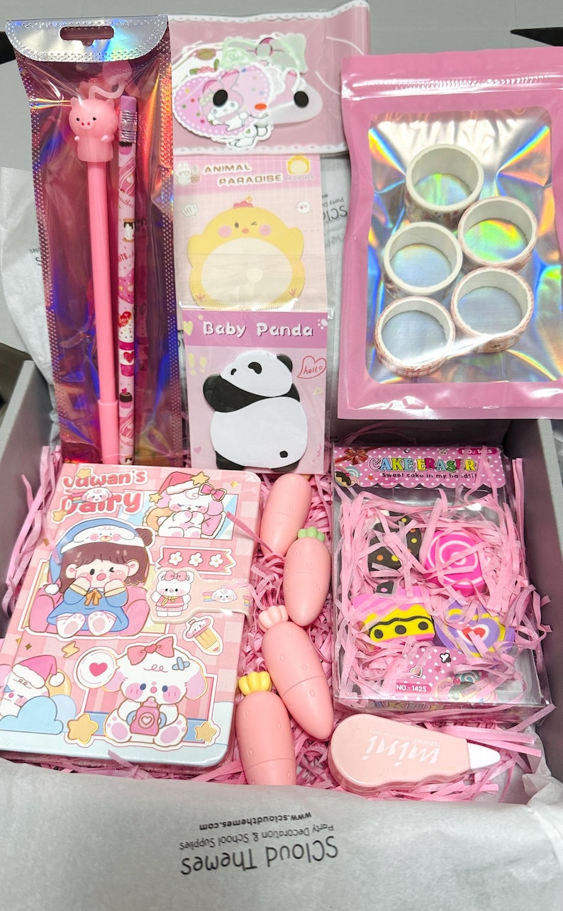 Op de afbeelding: Een briefpapier-cadeaubox met een roze pen met varkentje, een potlood, een Baby Panda notitieblok, vijf rollen washi-tape, een Yawan's Fairy notitieboek, vier wortelvormige items, een doosje taartvormige gummen en een mini correctietape.