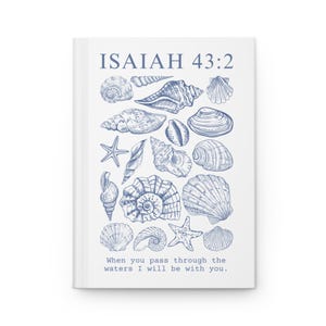 May include: A white journal with a blue illustration of various seashells and starfish. The text "ISAIAH 43:2" is at the top, with the quote "When you pass through the waters I will be with you" at the bottom.