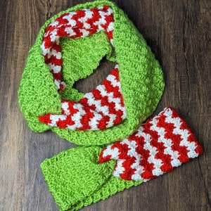 Puede incluir: Una bufanda de crochet verde y roja con un patrón a rayas. La bufanda está doblada por la mitad y los extremos están atados.