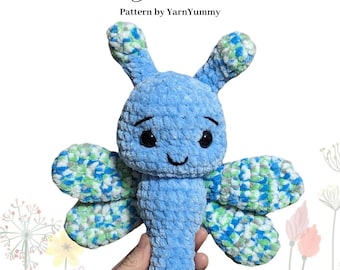 May include: A crocheted blue butterfly plush toy with green and white wings. The toy is held in a hand and has a smiling face. The text "Low Sew Butterfly Plushie" and "Pattern by YarnYummy" is visible in the image.