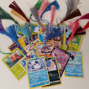 May include: A collection of Pokemon trading cards with colorful tassels attached. The cards feature various Pokemon characters and abilities.