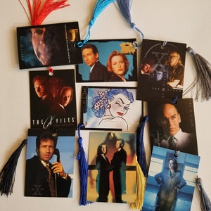 May include: A set of nine bookmarks featuring characters and imagery from the television show "The X-Files". The bookmarks are printed on cardstock and have colorful tassels.