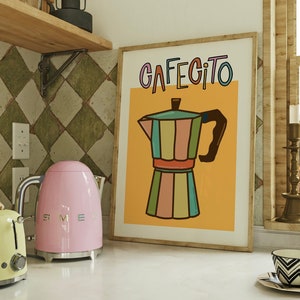 Può includere: Una stampa incorniciata con sfondo giallo e la parola "CAFEGITO" in lettere colorate. Una caffettiera a righe colorate si trova al centro della stampa.