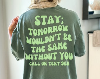 May include: Green t-shirt with a light green graphic that says "STAY: TOMORROW WOULDN'T BE THE SAME WITHOUT YOU CALL OR TEXT 988"