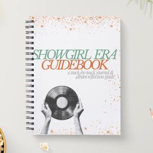 May include: A white spiral-bound notebook with the title "SHOWGIRL ERA GUIDEBOOK" in green and orange. The cover features a black and white illustration of hands holding a vinyl record. The notebook is a track-by-track journal and album reflection guide.