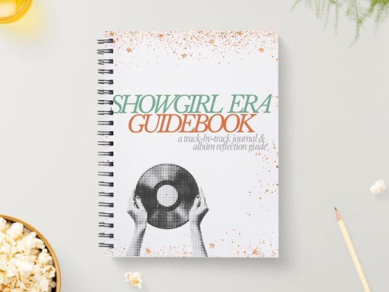 May include: A white spiral-bound notebook with the title "SHOWGIRL ERA GUIDEBOOK" in green and orange. The cover features a black and white illustration of hands holding a vinyl record. The notebook is a track-by-track journal and album reflection guide.