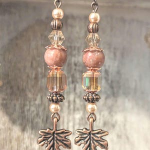 May include: A pair of dangle earrings with a copper leaf charm, pink and clear glass beads, and copper accents.