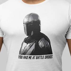 May include: A white t-shirt with a black and white image of a Mandalorian character. The text "You had me at battle droids" is printed on the shirt.