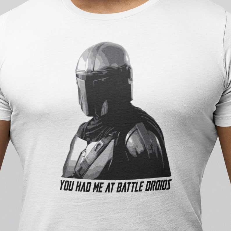 May include: A white t-shirt with a black and white image of a Mandalorian character. The text "You had me at battle droids" is printed on the shirt.