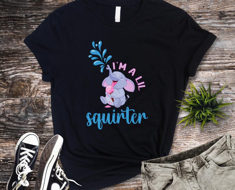 May include: Black t-shirt featuring a cartoon elephant squirting water and holding ice cream. The text "I'm a lil squirter" is in blue and pink. The shirt is paired with black sneakers and gray jeans.