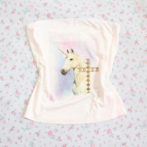May include: A white tube top featuring a unicorn graphic with a gold cross. The unicorn is white with a golden horn, set against a pastel background. The top is made of a soft, light fabric.