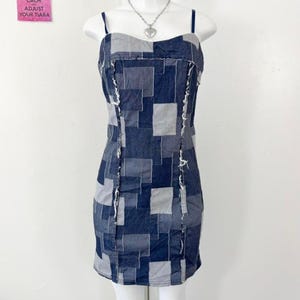 Peut inclure: Mini-robe en patchwork de denim, avec un motif carré dans des tons de bleu et de gris. La robe a de fines bretelles et une silhouette ajustée. Les bords effilochés ajoutent une touche vintage.