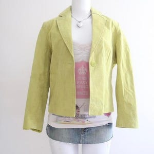 Peut inclure: Un blazer vert clair à bouton unique. Le blazer est porté sur un haut blanc avec le texte "IT'S NOT EASY BEING A PRINCESS". Une jupe en jean et un pantalon blanc complètent la tenue.