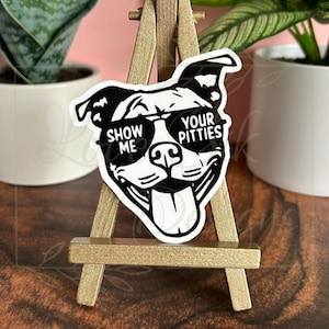 May include: Black and white sticker of a pit bull wearing sunglasses with the text "Show Me Your Pitties".