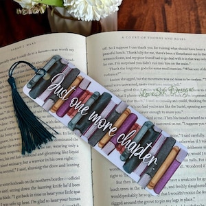 May include: A bookmark featuring a stack of colourful books with the text "Just one more chapter." The bookmark is white with a watercolour-style illustration of the books.