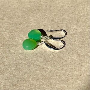 May include: A pair of silver earrings with green gemstone drops. The earrings have a simple design and are perfect for everyday wear.