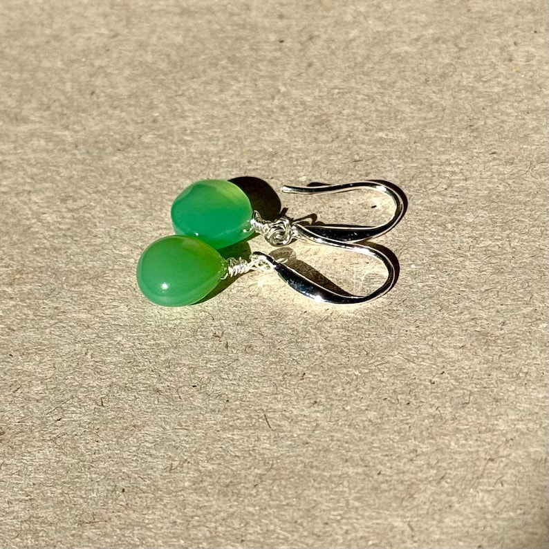 May include: A pair of silver earrings with green gemstone drops. The earrings have a simple design and are perfect for everyday wear.