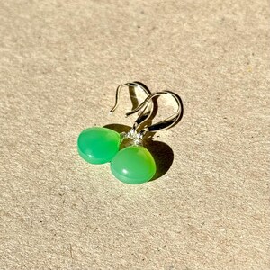 May include: A pair of silver dangle earrings with green gemstone drops. The earrings have a simple design and are perfect for everyday wear.