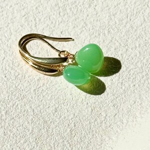 May include: Gold earrings with green gemstone drops. The earrings have a simple, elegant design.
