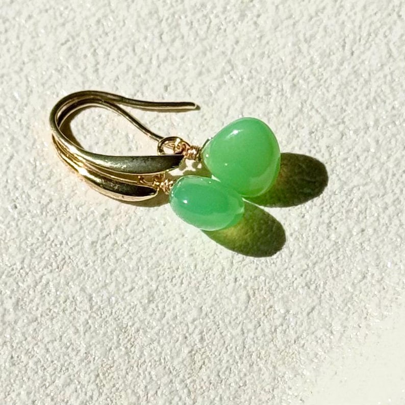 May include: Gold earrings with green gemstone drops. The earrings have a simple, elegant design.