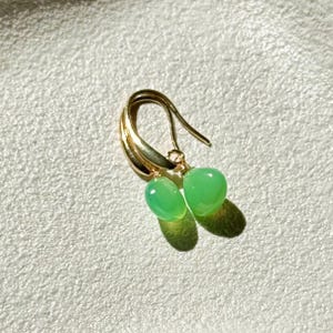 May include: A pair of gold earrings with green gemstone drops. The earrings have a simple, elegant design.