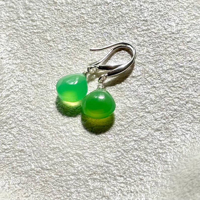 May include: A pair of silver earrings with green gemstone drops. The earrings have a simple design and are perfect for everyday wear.