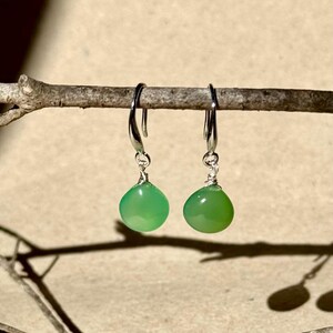 May include: A pair of silver dangle earrings with green gemstone drops. The earrings are hanging from a branch.