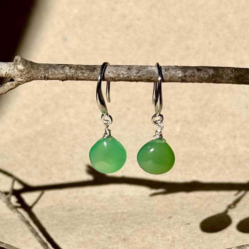 May include: A pair of silver dangle earrings with green gemstone drops. The earrings are hanging from a branch.