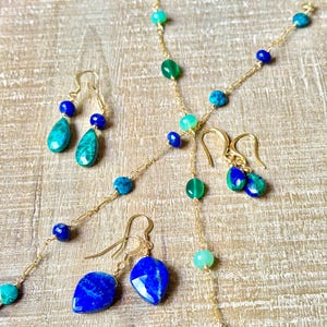 May include: A selection of gold-coloured jewellery, including necklaces and earrings. The necklaces and earrings are decorated with various gemstones in shades of blue and green. The earrings are teardrop-shaped.