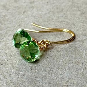 May include: A pair of gold earrings with green gemstone drops. The earrings have a simple, elegant design.