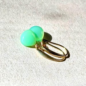 May include: A pair of green gemstone earrings with gold wire wrapped around the stones and gold hooks.
