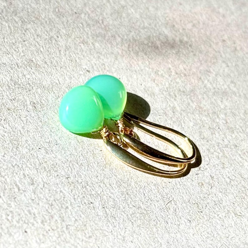 May include: A pair of green gemstone earrings with gold wire wrapped around the stones and gold hooks.