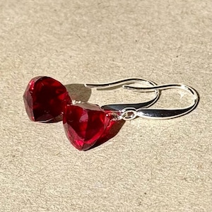 Puede incluir: Un par de pendientes de plata con gotas de piedras preciosas rojas. Las piedras preciosas son facetadas y tienen forma de lágrima.